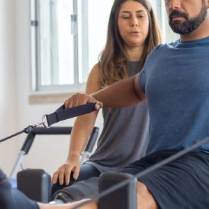 Hombre haciendo pilates en una máquina supervisado por una mujer