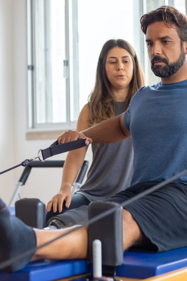 Hombre haciendo pilates en una máquina supervisado por una mujer